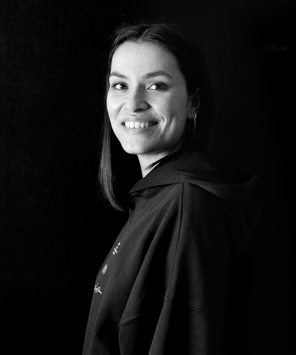 Schwarz-weiß Portrait von Teammitglied Katja Müller, junge lächelnde Frau kurzen Haaren, Blick über die Schulter in die Kamera