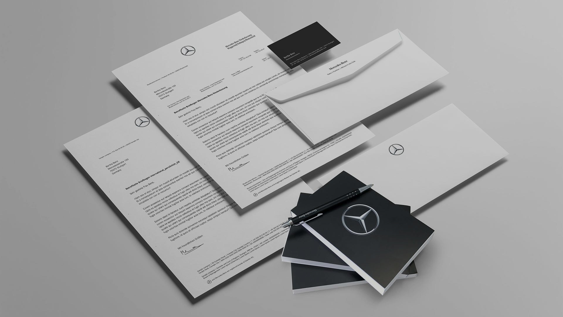 Briefbögen, Visitenkarten, Umschläge und ein Kugelschreiber mit Mercedes-Benz Logo auf grauem Hintergrund